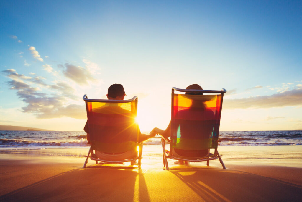 Couple sitting in beach chairs and holding hands.