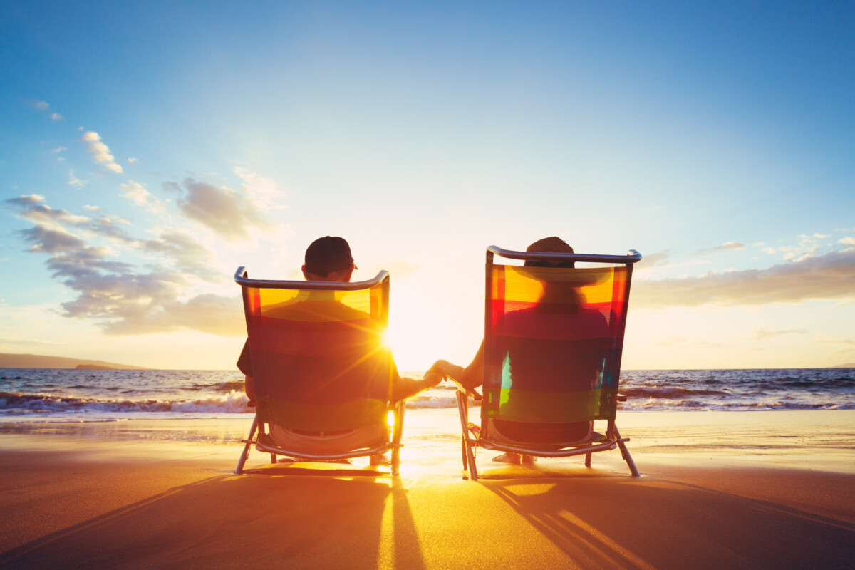 Couple sitting in beach chairs and holding hands.