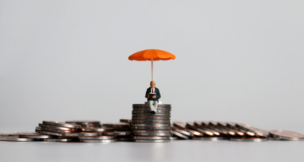 Stack of coins with a tiny person sitting on top holding an orange umbrella