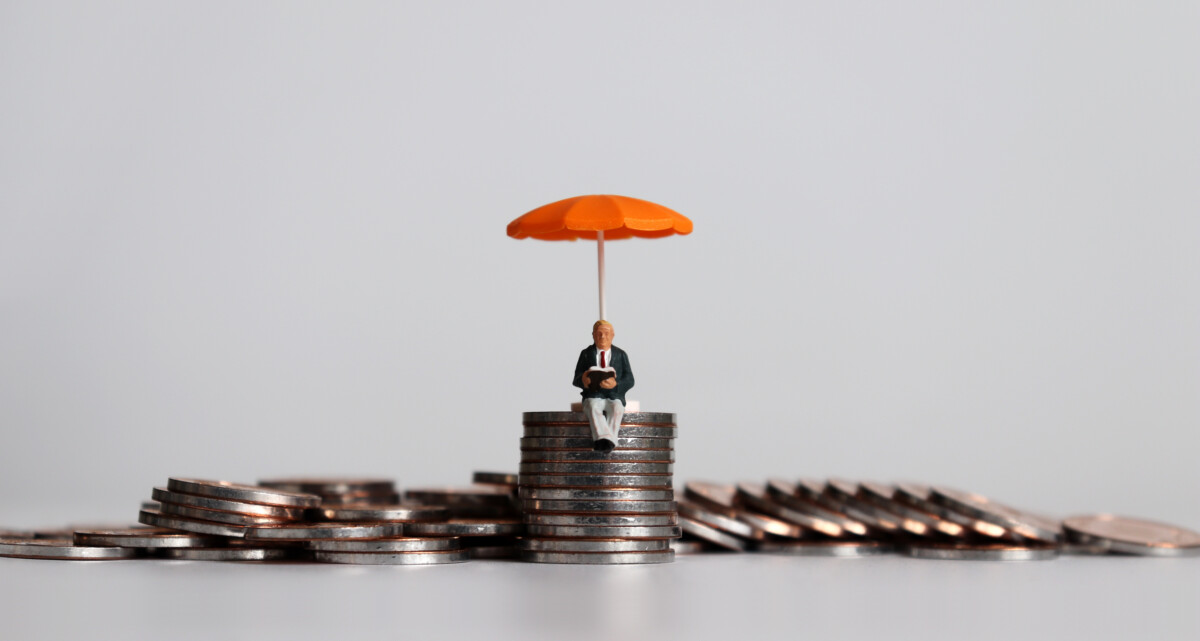 Stack of coins with a tiny person sitting on top holding an orange umbrella