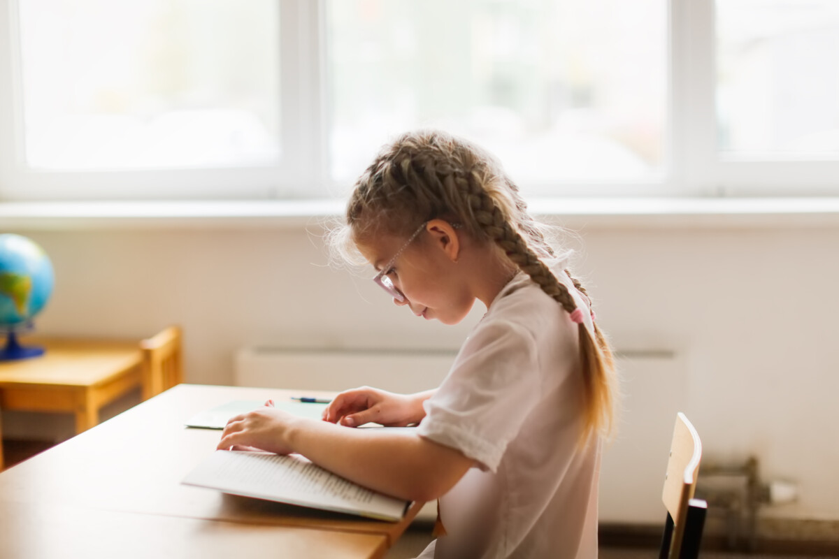 Schoolgirl reading a book at a desk in a classroom