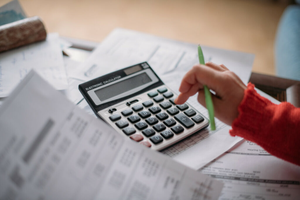 The hands of an elderly woman with a calculator and a lot of utility bills.