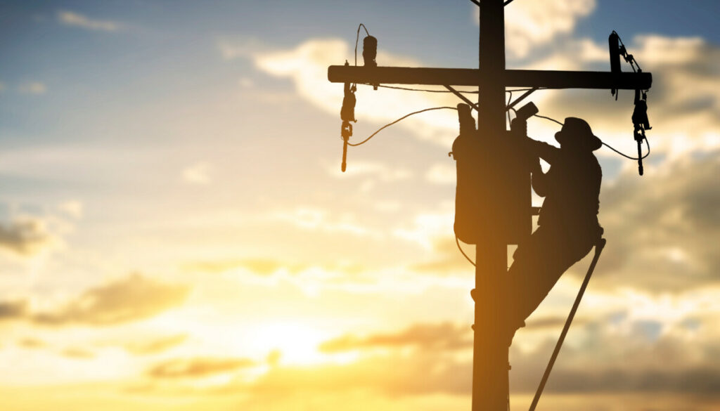 Silhouette of man working on a power line