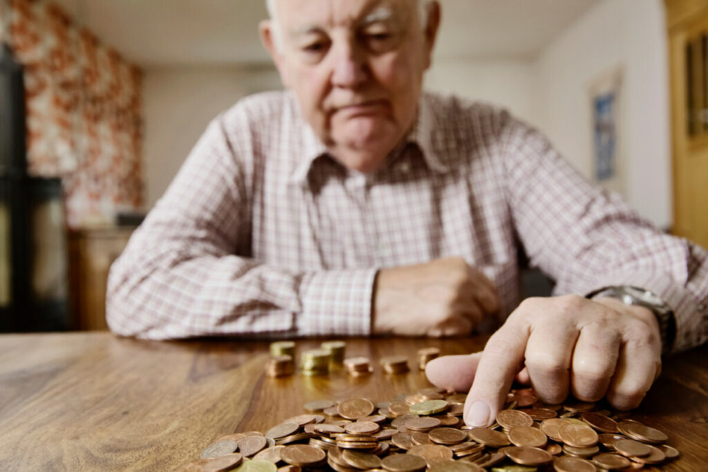 Senior man seated at a table counting pennies.