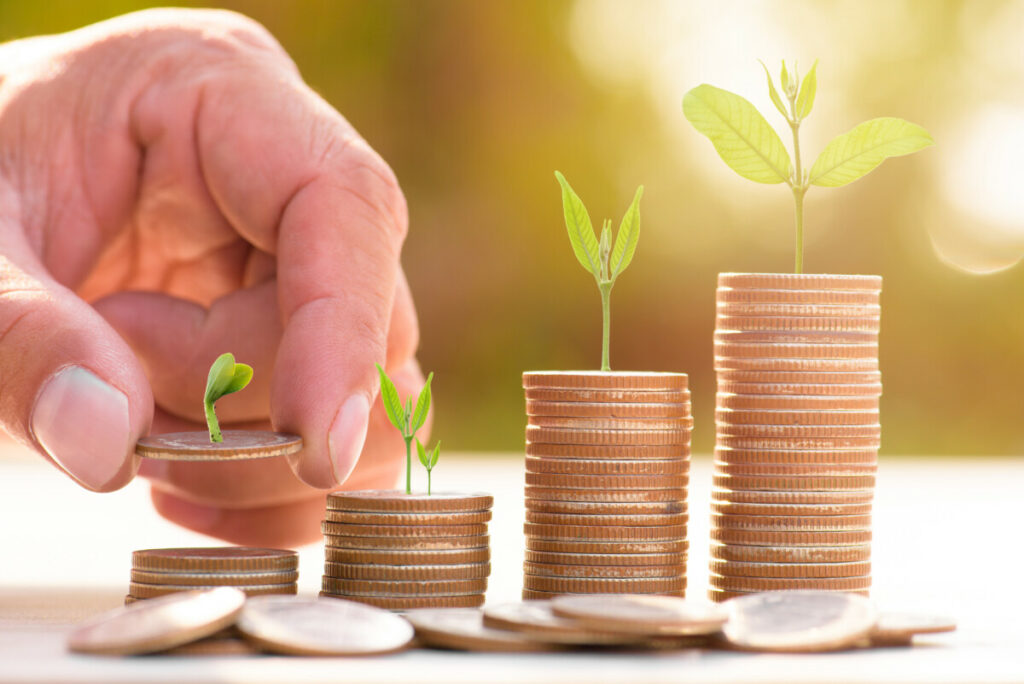 Stacks of coins with plants buds growing on top of each and a finger counting them.
