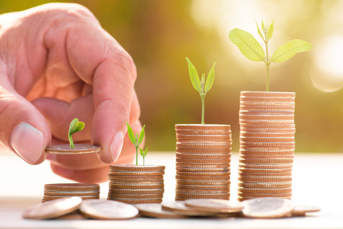 Stacks of coins with plants buds growing on top of each and a finger counting them.