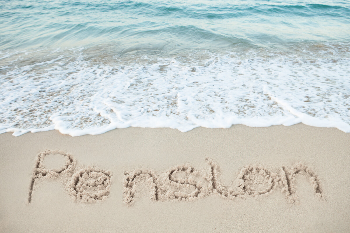 Sand by the water's edge at the beach, which the letters "Pension" written in the wet sand.