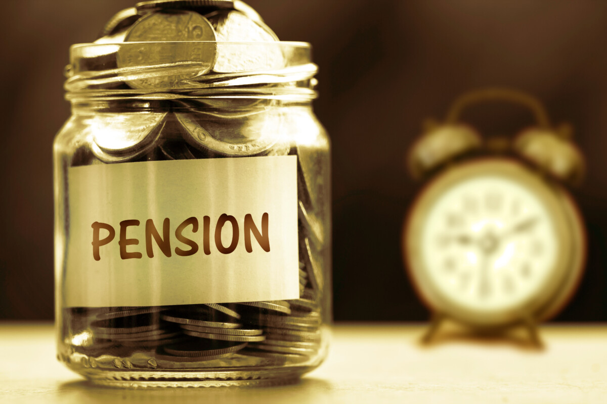 Jar labeled "pension" full of coins with an alarm clock in the background