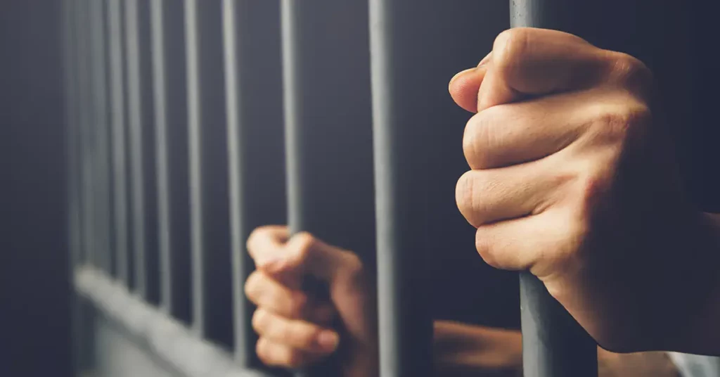 image of a mans hands holding the bars of a jail cell representing how a criminal record affects immigration status