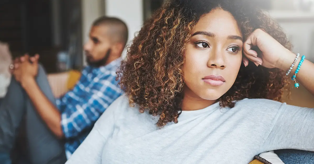 image of a woman close up on the couch looking away upset with her ex partner in the background