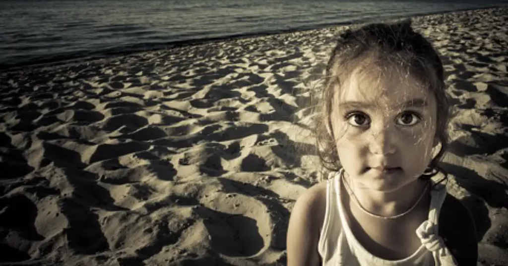 young girl alone on a beach with ocean behind her