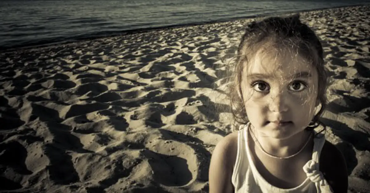 young girl alone on a beach with ocean behind her