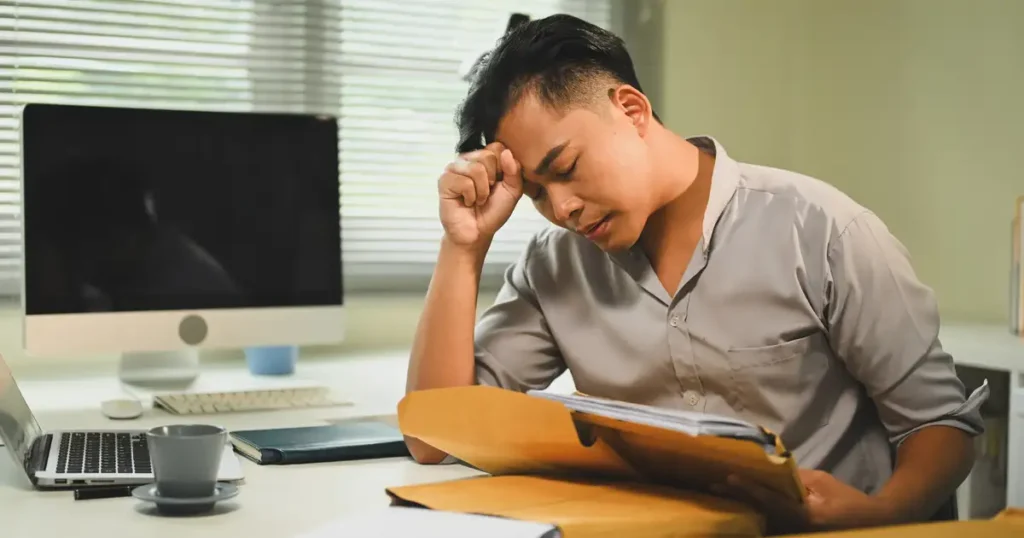A person is sitting at a cluttered desk, visibly frustrated as they sift through a pile of complex legal paperwork and medical documents related to a vaccine injury claim. The scene conveys the overwhelming nature of navigating vaccine injury law and the need for experienced attorneys to assist with filing claims and seeking compensation for medical expenses and injuries.