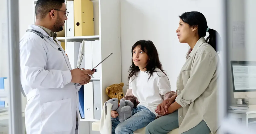 In the image, a civil surgeon is conducting a pediatric medical examination, carefully documenting the child's vaccination records. The setting reflects a professional medical environment, emphasizing the importance of vaccination assessment for immigration purposes and adherence to vaccination requirements.