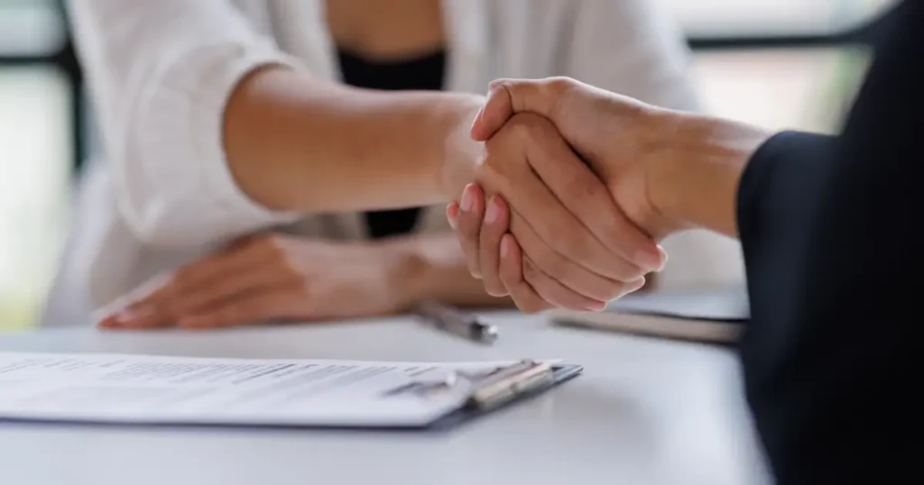 In a professional office setting, an attorney and a client are engaged in a handshake, symbolizing their partnership in navigating a vaccine injury claim. This moment reflects the attorney's commitment to representing clients affected by vaccine-related injuries in the pursuit of compensation.