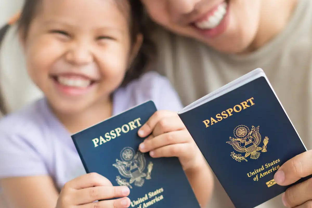 A smiling child and parent proudly holding U.S. passports, symbolizing family immigration and the challenges families face navigating vaccine requirements and exemptions for children in the immigration process.