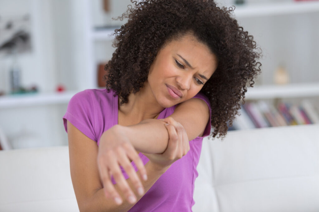 Woman holding painful elbow at home, possible SIRVA after vaccination