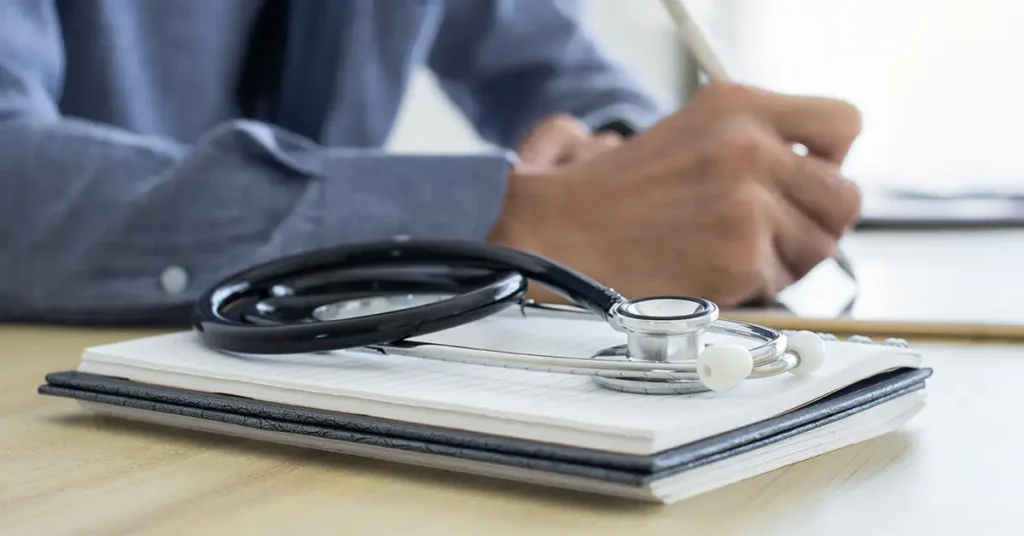 Stethoscope on notebook, civil surgeon writing on an immigration vaccine waiver document.
