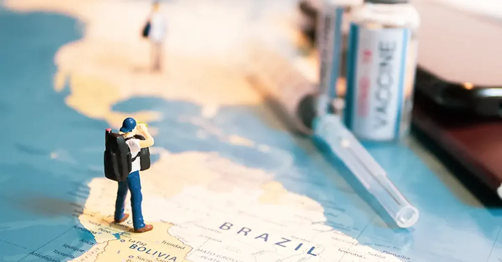 A miniature traveler figurine stands on a world map beside vaccine supplies, illustrating global travel issues that immigration attorneys help clients address.