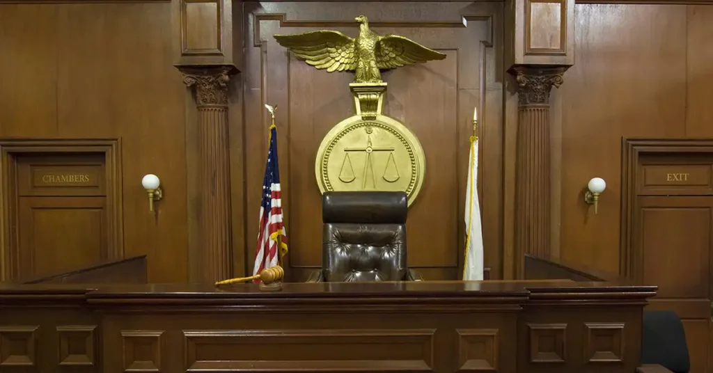 Empty courtroom with judge’s bench and scales of justice, symbolizing the legal system used to resolve vaccine injury claims