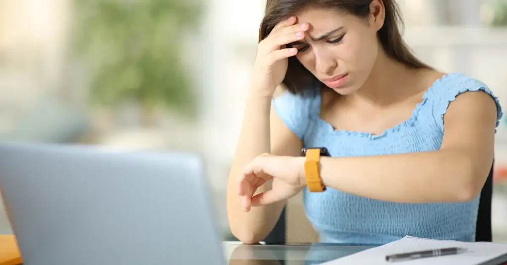 Woman looking at her watch while working at a desk, representing delays and uncertainty often experienced during the vaccine injury claims process
