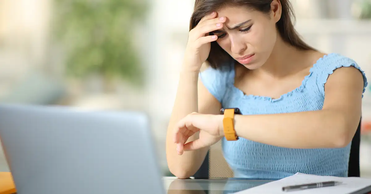 Woman looking at her watch while working at a desk, representing delays and uncertainty often experienced during the vaccine injury claims process