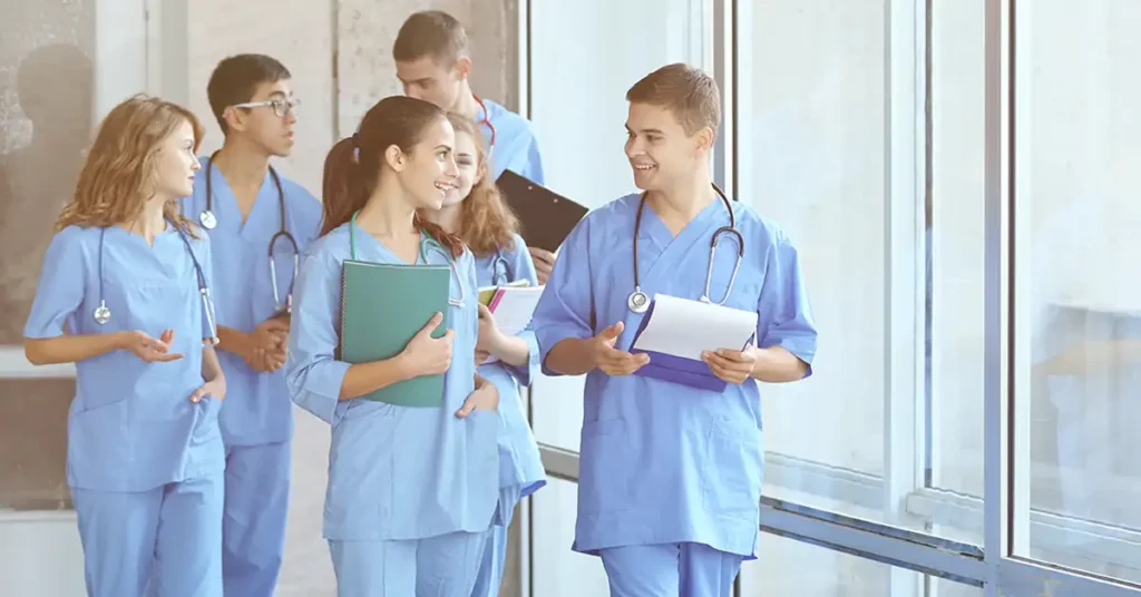 Medical students in scrubs discussing paperwork in a hospital hallway, clinical rotation exemption support