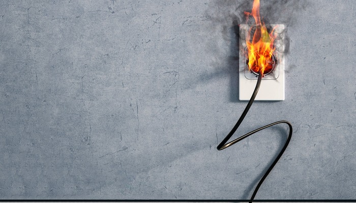 Electrical plug overheating and catching fire in wall outlet, representing dangerous and defective consumer products that may lead to product liability litigation.