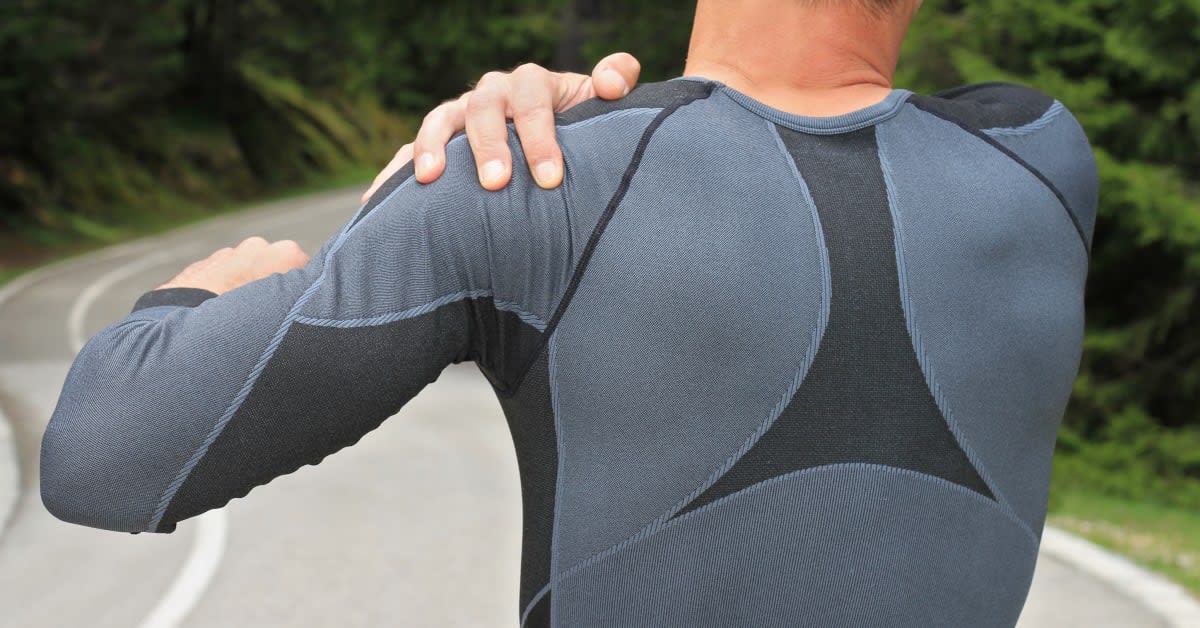 Individual grasping a painful shoulder while outdoors, representing reduced range of motion and ongoing shoulder discomfort associated with a potential vaccine shoulder injury
