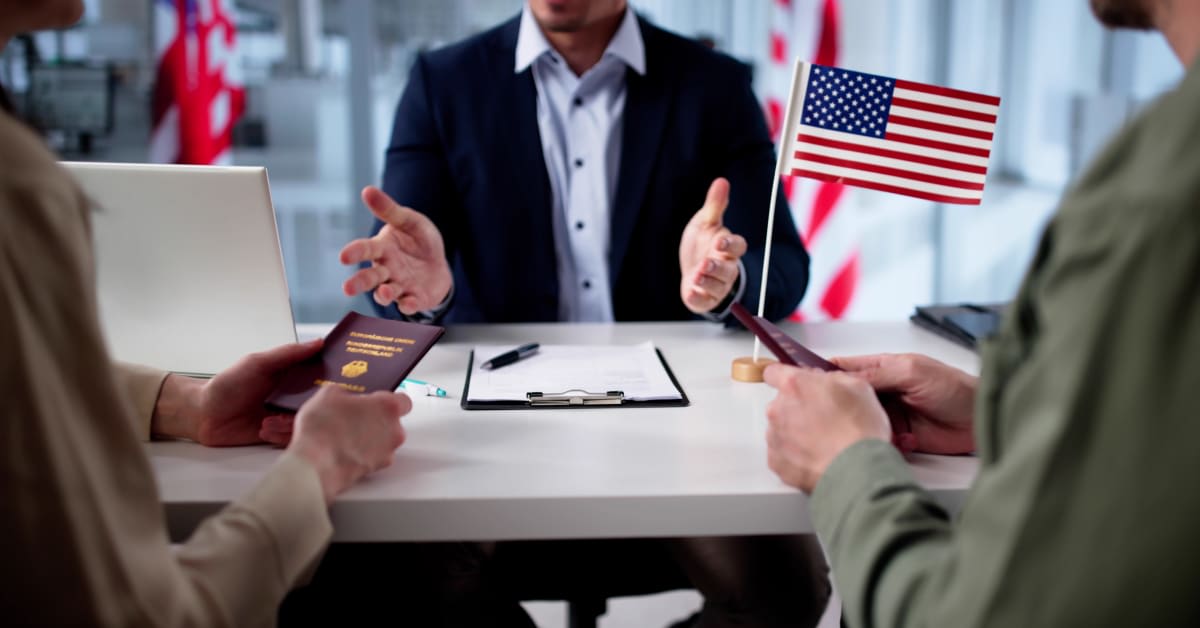An immigration attorney meeting with clients holding passports beside a U.S. flag, reflecting legal guidance for immigration matters.