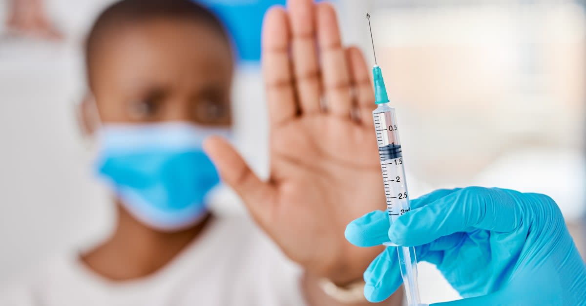 Masked employee holding up hand toward syringe, workplace vaccine exemption legal help
