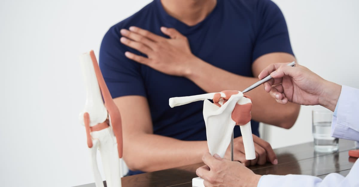 shoulder-pain-model Physician explaining a shoulder joint model to a patient experiencing shoulder pain during an orthopedic consultation related to a potential vaccine shoulder injury