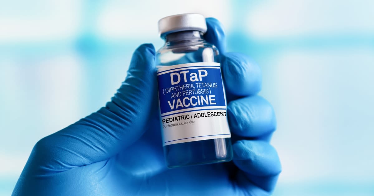 Gloved medical professional holding a DTaP vaccine vial for diphtheria, tetanus, and pertussis