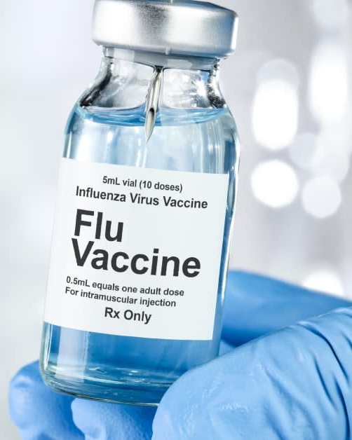 Flu vaccine vial held by a gloved medical professional for influenza vaccination