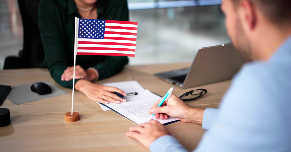 A person signing immigration paperwork beside a U.S. flag, representing consular processing matters assisted by immigration attorneys.