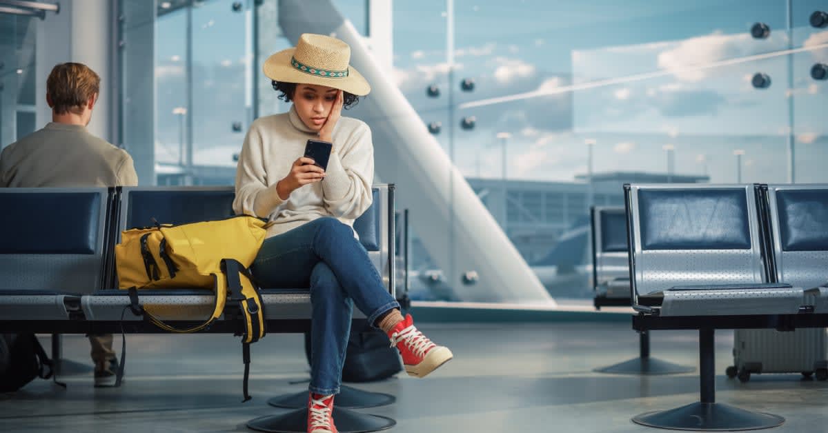 A traveler sitting in an airport terminal with a phone, representing immigration travel and waiting-period concerns handled by immigration attorneys.