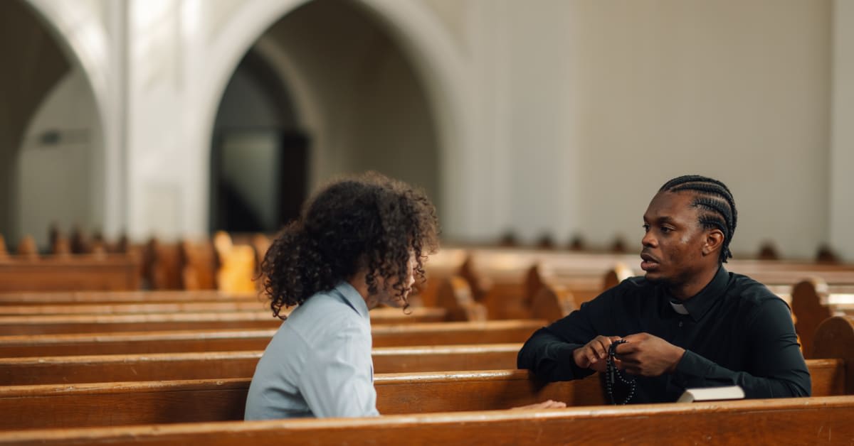 Individual discussing religious vaccine exemption concerns with clergy member in church